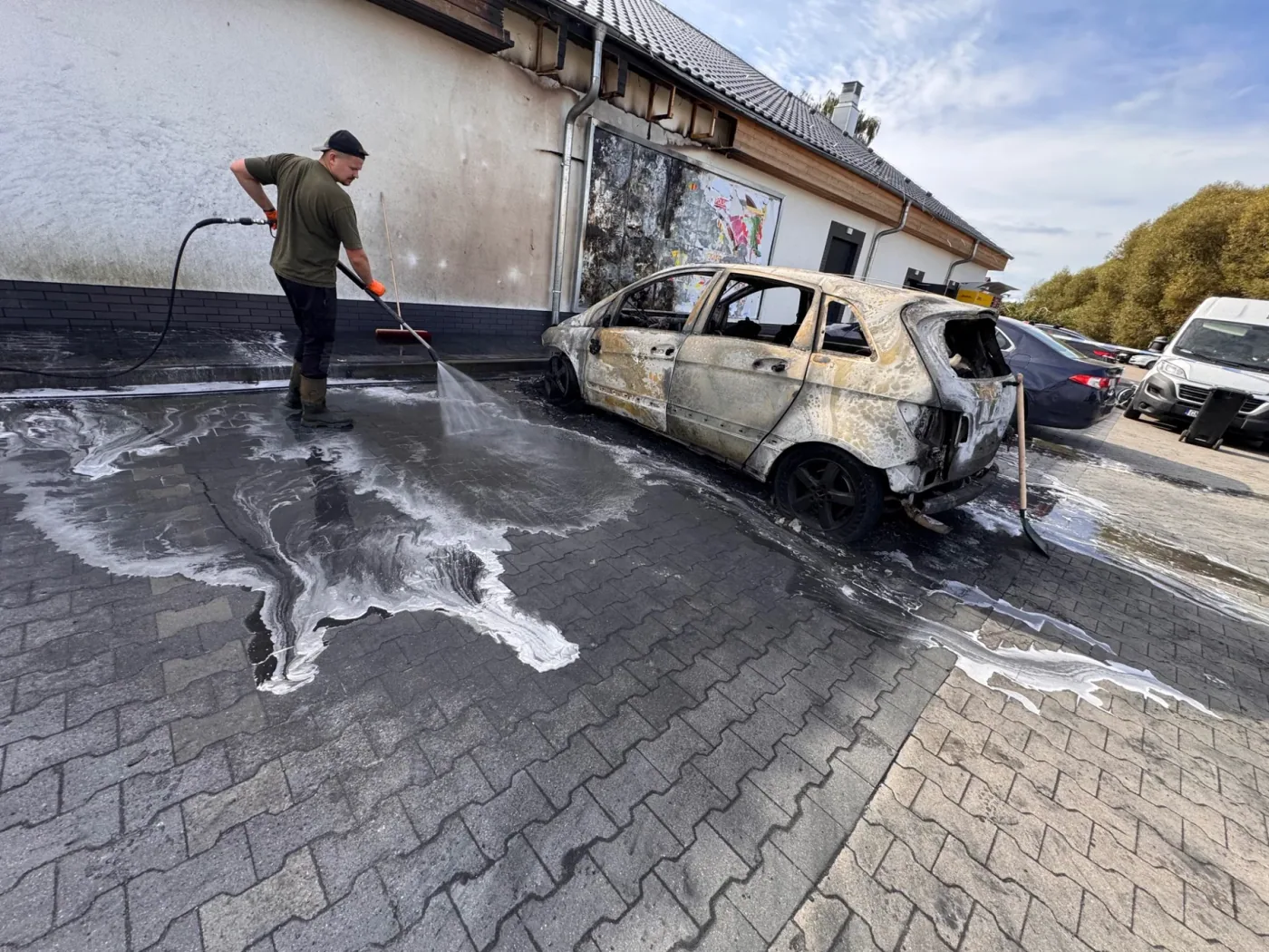 Mycie kostki brukowej obok pojazdu uszkodzonego przez pożar